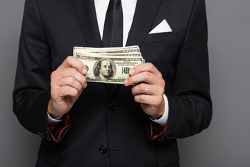 cropped view of middle aged businessman holding dollar banknotes isolated on grey