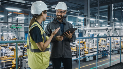 Male Specialist and Female Car Factory Engineer in High Visibility Vests Using Tablet Computer. Automotive Industrial Manufacturing Facility Working on Vehicle Production. Diversity on Assembly Plant.