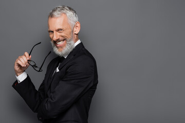 cheerful middle aged businessman holding glasses and smiling on grey