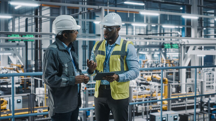 Multiethnic Manager and African American Car Factory Engineer in Uniform Using Tablet Computer. Automotive Industry 4.0 Manufacture Employees Discuss Work on Vehicle Assembly Plant.