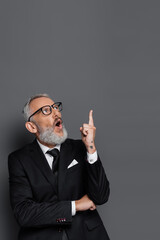 surprised middle aged businessman in glasses pointing with finger isolated on grey