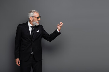 side view of angry middle aged businessman in glasses gesturing isolated on grey
