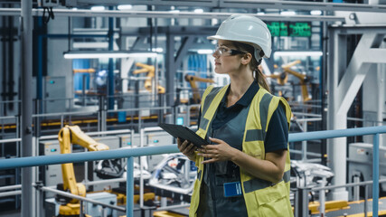 Female Car Factory Engineer in High Visibility Vest Using Tablet Computer. Automotive Industrial Manufacturing Facility Working on Vehicle Production with Robotic Technology. Automated Assembly Plant.