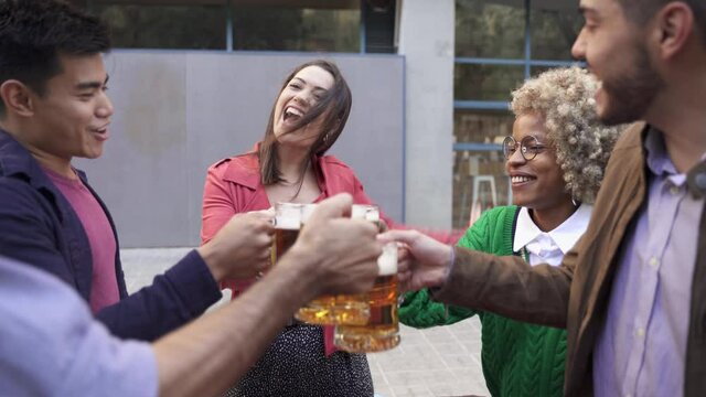 Carefree friends enjoying drinking together in outdoors bar. Group of happy multiracial friends toasting beer to celebrate after work or birthday