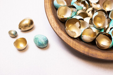 A festive Easter background with lots of golden eggshells and beautiful, modernly colored eggs. Golden eggs as a concept of wealth and success. An original idea for handmade Easter decor. Copy space.
