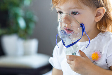 Cute toddler girl are sitting and holds a nebulizer mask leaning against the face, concept airway...