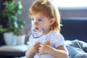 Cute toddler girl are sitting and holds a nebulizer mask leaning against the face, concept airway treatment - obrazy, fototapety, plakaty