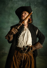 Cropped portrait of brutal man, medeival pirate in vintage costume with pistol, gun isolated over...