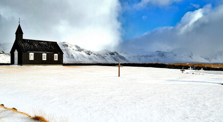 black church in Budir stone fence and in the background snow-capped and misty mountains, Iceland
