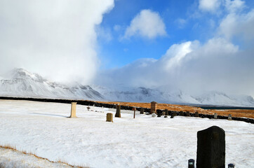 cemetery in Budir stone fence and tombstones in the background snow-capped and misty mountains, Iceland