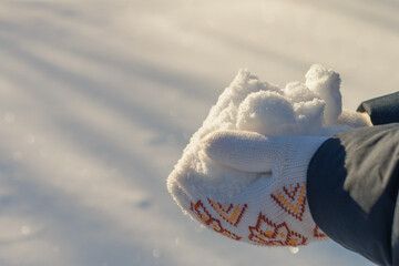 hands holding a pile of clean sparkling snow, wearing white knitted mittens, sun shining, bright heap, sunny winter day, snowy background with light beams, streaks, lines, ice crystals, snowflakes