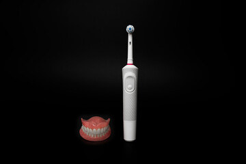 Dental care with an electric brush. Dentures and an electric brush on a black background. Acrylic...