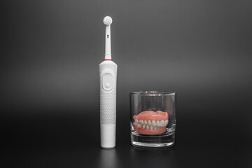 Dental care with an electric brush. Dentures and an electric brush on a black background. Acrylic...