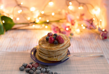 Delicious American pancakes with syrup and berries, blueberries, raspberries on a pink background with flowers with blur bokeh 