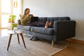 Obraz premium Wide shot of young man taking picture to laptop screen on the sofa