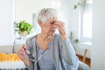Senior woman in glasses rubs her eyes, suffering from tired eyes, ocular diseases concept