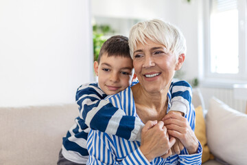 Happy senior grandmother sit on couch in living room hugging cute little preschooler grandson, smiling mature 70s granny embrace cuddle with small grandchild, show love and care, bonding concept