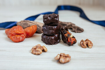  Dark chocolate sweets with nuts, caramel and fruits on wooden background.
