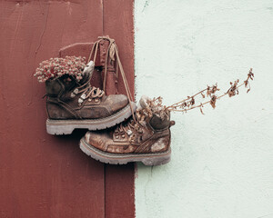 Old shoes are hanging on the wall. Flowers in old shoes. The decor is in the yard. Black and brown wall. Unusual decor.