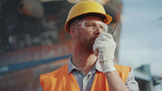 Serious man shipbuilder in uniform talking into walkie-talkie outdoors