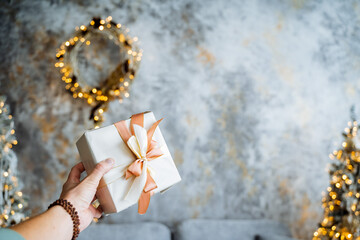 A big gift box with a lush bow on a festive background. Glare from the garland and wreath of spruce branches. Christmas decorations and Christmas and New Year's mood.