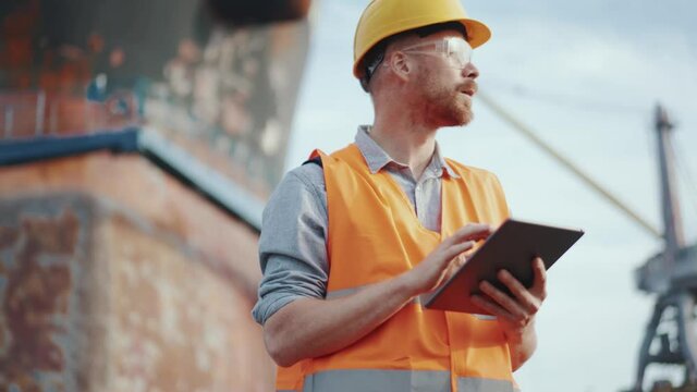 Confident man shipbuilder in uniform typing at tablet outdoors
