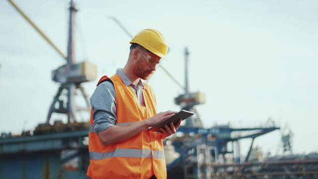 Side view of man shipbuilder in uniform typing at tablet outdoors