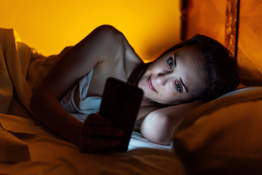 beautiful middle aged young woman lying in bed reading smartphone. insomnia. screen addiction. watch movie