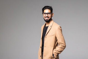 Portrait of a smart young indian man standing with arms crossed against gray background