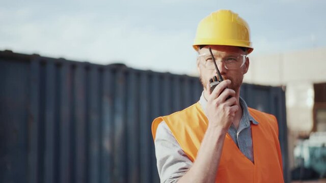 Confident man shipbuilder in helmet talking into walkie-talkie outdoors
