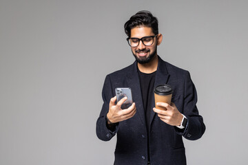 Handsome young indian man with backpack carrying cup of take away coffee and talking on phone when standing in office building