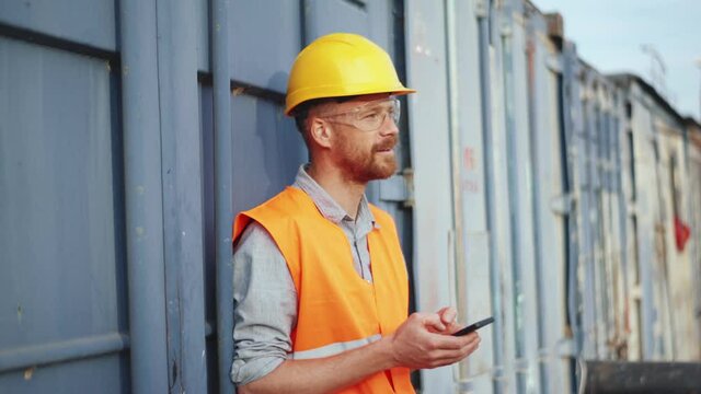 Smiling man shipbuilder in uniform texting by phone