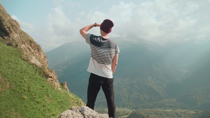 Rear view of a young man in a hat standing with his back against the background of mountains