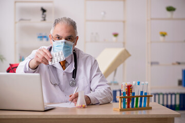 Old male doctor working in the clinic during pandemic