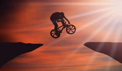 Fototapeta na wymiar Biker Jumping Over Mountain Cliff At sunset Orange sky and Sun shine Rays. Cyclist Big Jump From Dark Side To Light Side. Positive Healthy Life Style and happiness 
