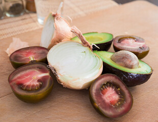 vegetables black tomatoes, avocado and onions on wooden board