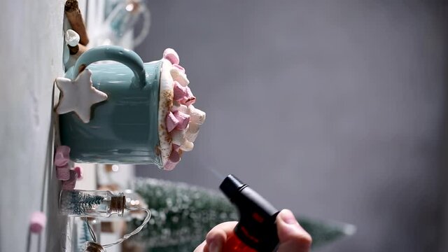 Christmas drink. Toasting marshmallows with butane kitchen torch for hot chocolate in blue mug and decoration. FullHD 25 fps vertical video footage