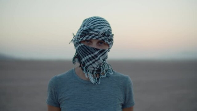 Portrait of woman wearing checkered keffiyeh standing in the desert looking at camera. Caucasian female tourist in desert.