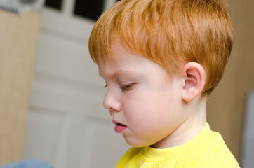 Portrait of a 4-year-old red-haired boy concentrating on something. Side view of a child with a serious expression