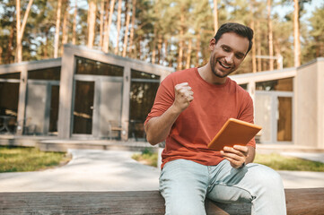 Joyful man with tablet gesturing with fist