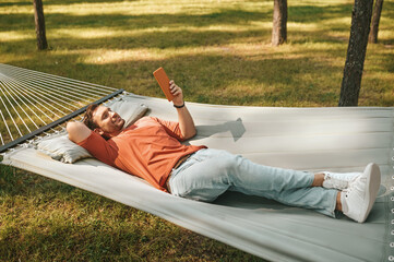 Happy man relaxing in hammock with tablet