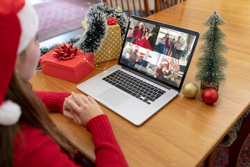 Naklejka na ściany i meble Caucasian woman in santa hat making christmas laptop group video call with family and friends