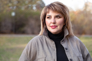 A beautiful curvy mature woman looks to the side. Female portrait of middle-aged person outdoors
