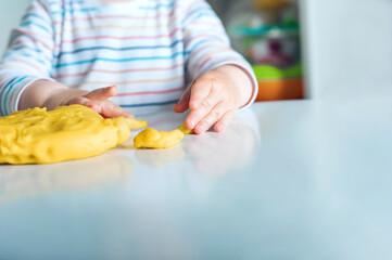 Toddler boy playing yellow plasticine Play-Doh in playroom close-up and copy space..