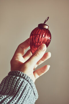 Woman's hand holding red Christmas tree decoration, minimalistic color scheme, lots of texture.