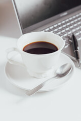 Cup of coffee and laptop on white table.