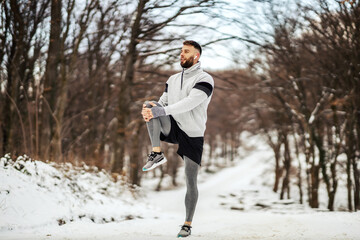 Sportsman doing stretching exercises and preparing to run in nature at snowy winter day. Winter fitness, sport, cold weather