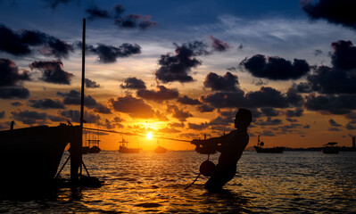 Silhouette of working fisherman and wooden boat.