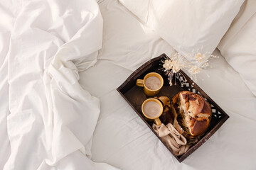 Breakfast on dark wooden vintage tray in bed with light beige sheet and pillows. Flat lay, top view. Slow romantic morning concept.