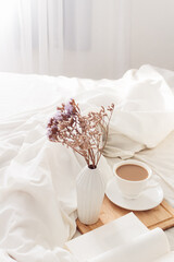 Breakfast on dark wooden vintage tray in bed with light beige sheet and pillows. Flat lay, top view. Slow romantic morning concept.